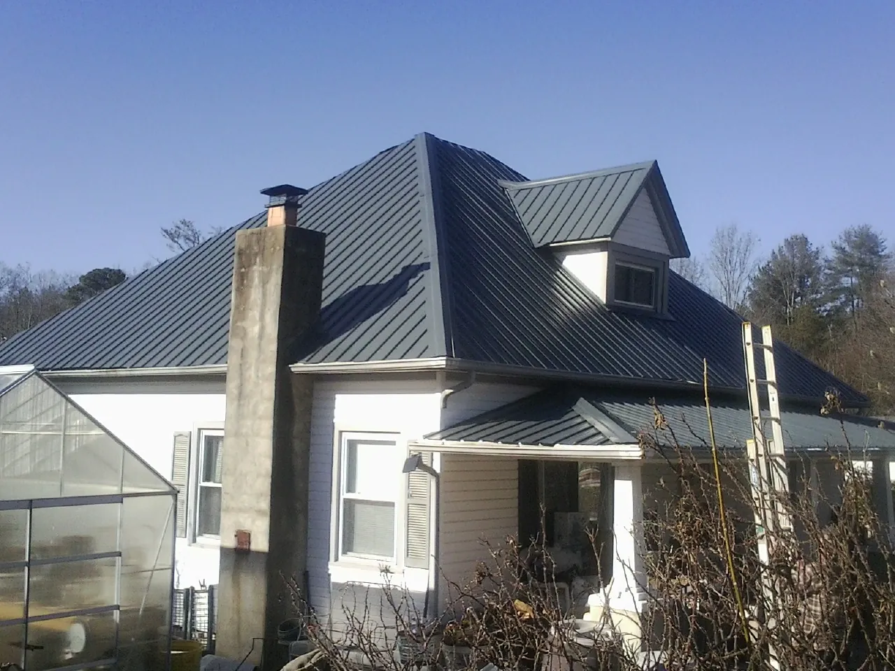 Dark blue standing seam metal roof on a white farmhouse with dormer — Slate & Tile Roof Repair by Roofing Brothers in Mequon