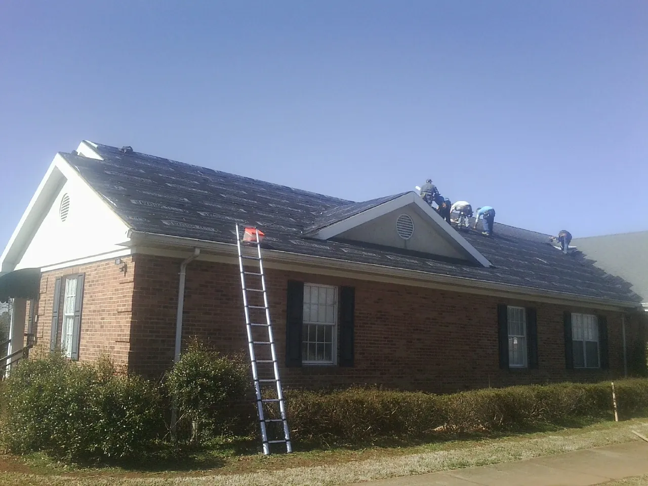 Crew tearing shingles off a brick ranch roof with a ladder set — Metal Roof Repair work by our crew in Mequon