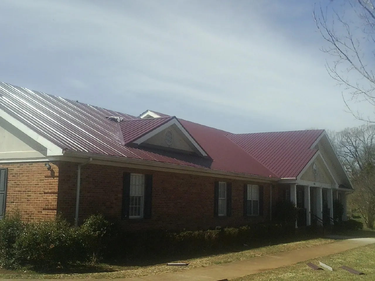 Red metal roof with gabled entries on a long brick building, from a Hail Damage Roof Repair job in Mequon