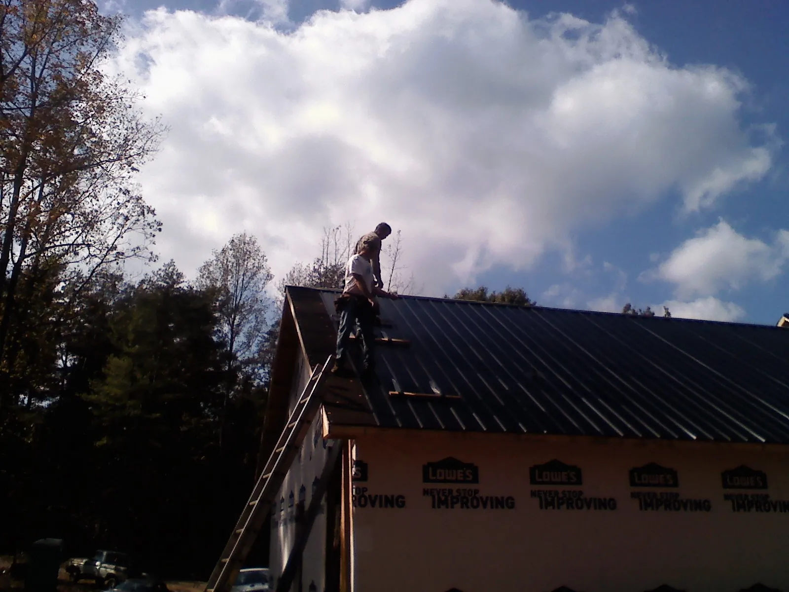 Roofer fastening dark metal panels high against a cloudy sky, from a Roof Inspection job in Mequon