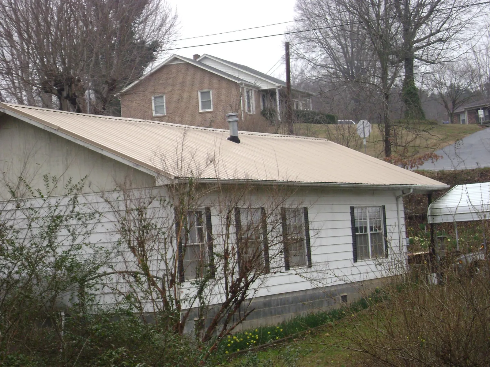 Tan metal roof on a white sided house set into a hillside — Commercial Roofing by Roofing Brothers in Mequon